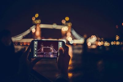 Cropped image of man photographing illuminated lamp at night