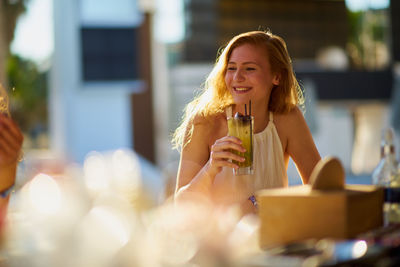 Smiling young woman sitting with drink during sunset