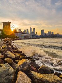 Sea by cityscape against sky during sunset