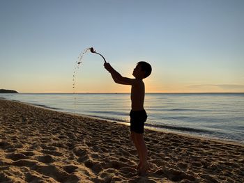 Full length of boy on beach against sky during sunset