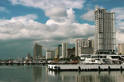 View of harbor with boats and buildings against cloudy sky