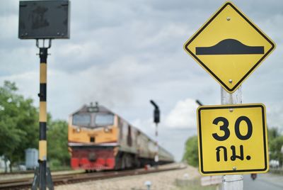 Close-up of speed bump sign by train on railroad track against sky