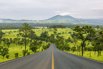 Road amidst trees and landscape against sky