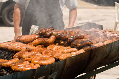 Midsection of man cooking chorizos on barbecue in city