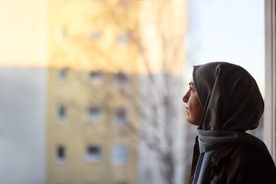 Thoughtful woman in headscarf looking through window