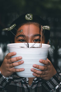 A young girl wearing a plaid shirt holding up a white potted plant in front of her face 