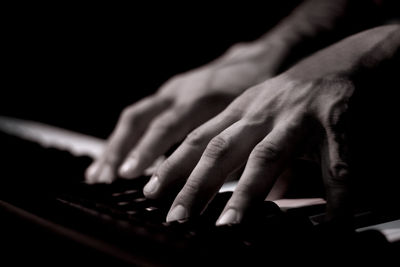 Tattooed mans hands on the keyboard of a piano. dark background