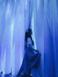 Woman standing against blue curtain