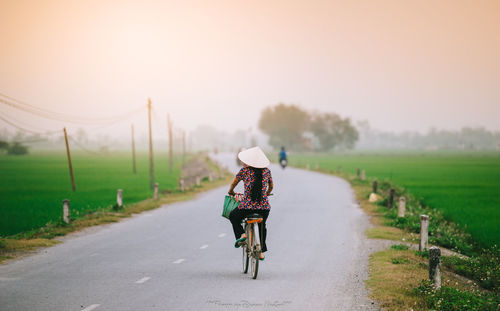 Rear view of woman riding bicycle on road against sky