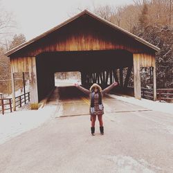 Young woman in warm clothing with arms raised standing on road during winter