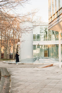 Man walking on footpath by street against buildings