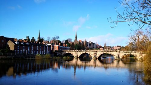 Arch bridge over river by buildings against blue sky