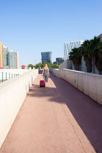 Rear view of a young traveler woman carrying a red trolley in the city