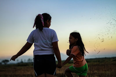 Friends standing on field against sky during sunset