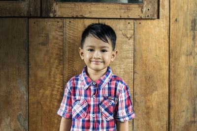 Portrait of smiling boy standing against wood