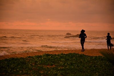 Silhouette woman running at beach during sunset
