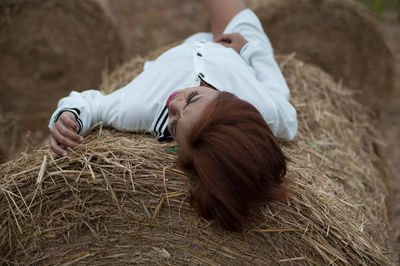 High angle view of young woman lying on hay bale at farm