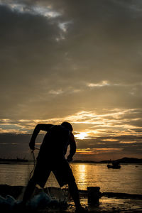 Silhouette fisherman with net on jetty at sea