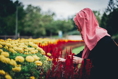 Side view of woman touching flowers at park