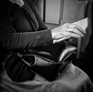 Midsection of woman with handbag reading magazine