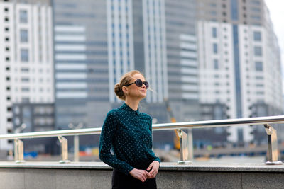 Young woman wearing sunglasses on railing in city