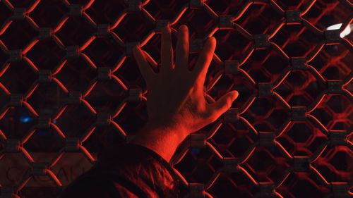 Cropped hand of man touching fence with illuminated red light at night