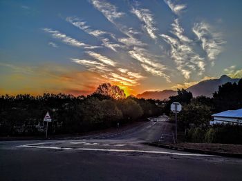 Road by trees against sky during sunset