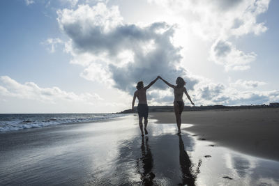 Couple walking at beach against sky
