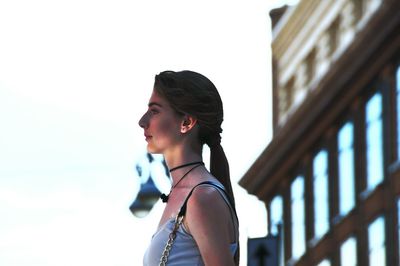 Side view of serious mature woman looking away while standing against sky in city