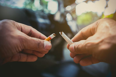 Cropped hands of man breaking cigarette outdoors