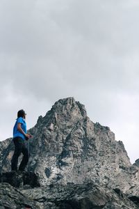 Man on rock by mountain against sky