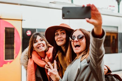 Happy friends taking selfie while standing on station