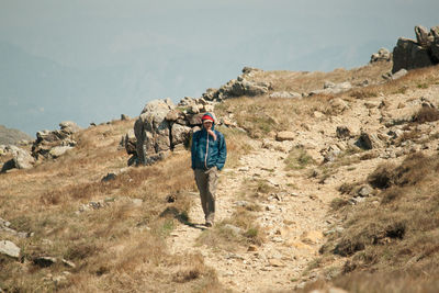 Rear view of man walking on landscape against sky