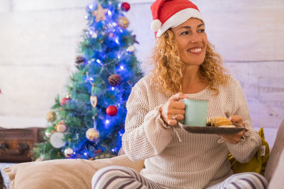 Full length of smiling woman sitting by christmas tree