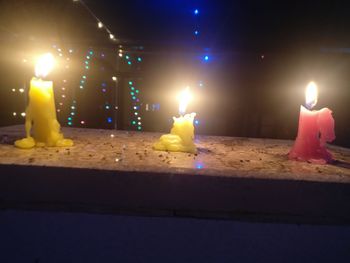 Close-up of lit candle on retaining wall at night