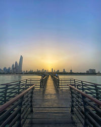 Pier over city against sky during sunset