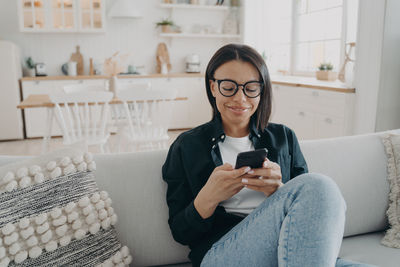 Young woman using mobile phone while sitting on sofa at home