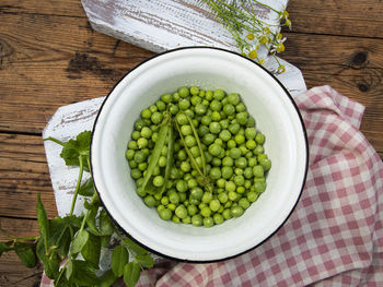 Fresh green peas in a white bowl, pods, on the table