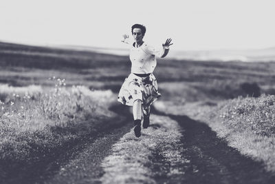 Woman running on dirt road against clear sky