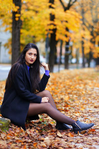 Young woman sitting on leaves during autumn