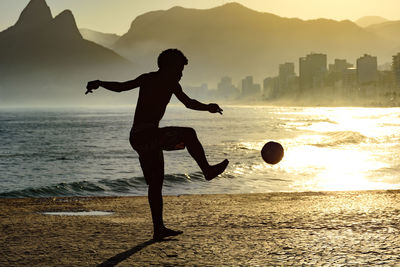 Silhouette man jumping on beach against sky during sunset