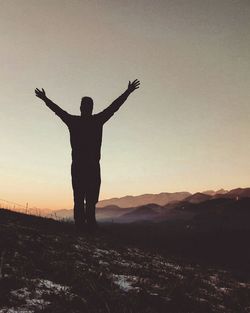 Silhouette woman with arms outstretched standing on field against sky