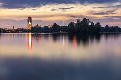 Scenic view of lake by buildings against sky during sunset