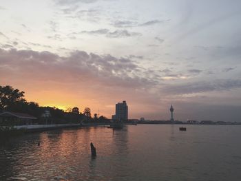 Silhouette buildings by river against sky during sunset