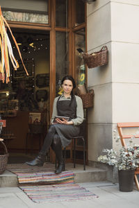 Portrait of owner holding digital tablet sitting at store entrance