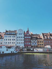 Buildings by river against clear blue sky