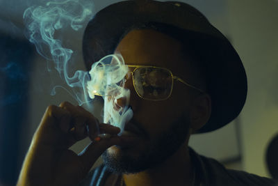 Close-up of man wearing hat smoking cigarette at home