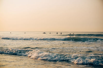 Scenic view of sea against clear sky during sunset and surfers surfing