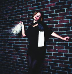 Beautiful woman holding liquor bottle against brick wall
