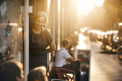 Portrait of smiling female employee standing at entrance of deli